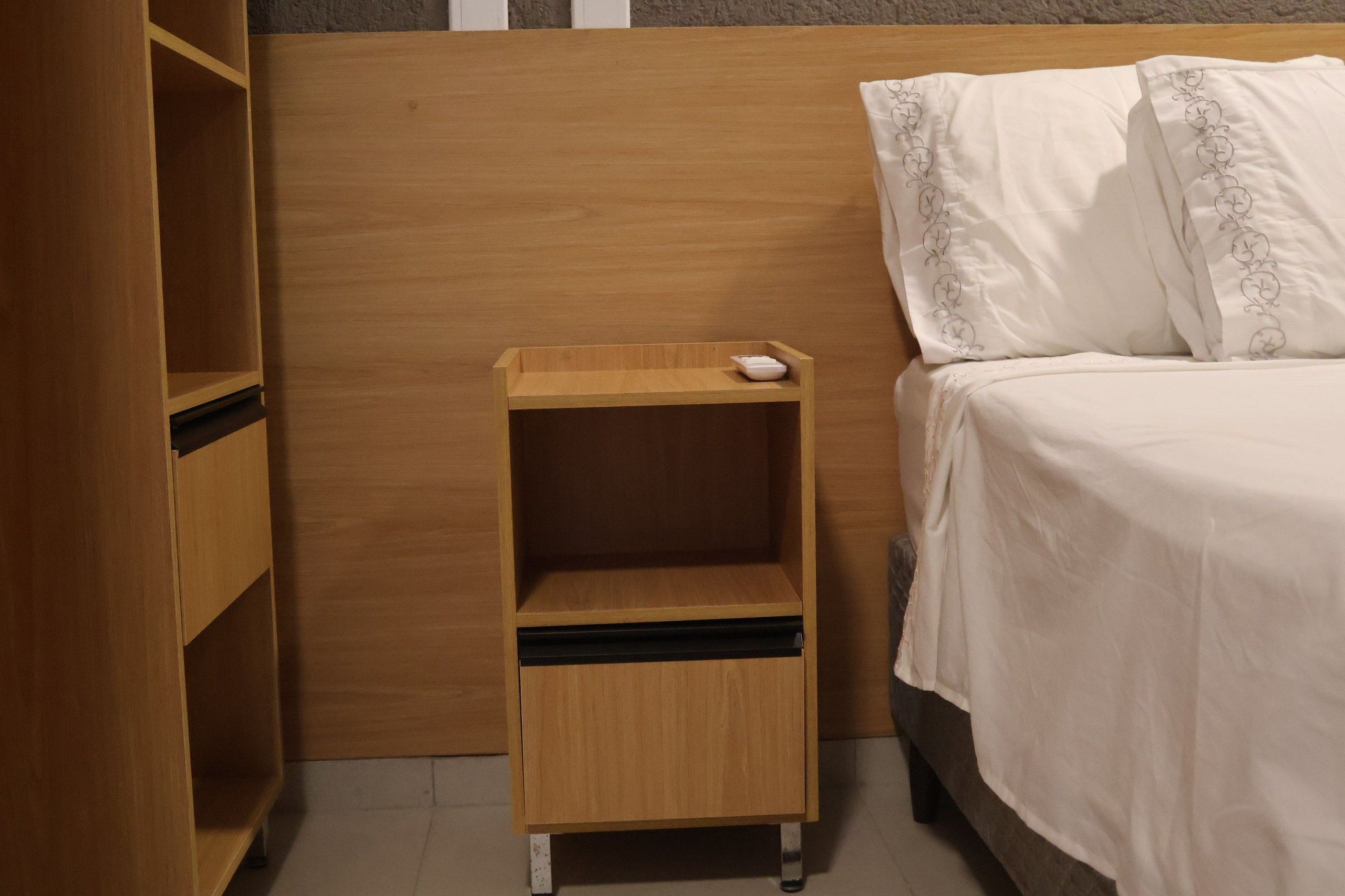 Una camera da letto con un comodino in legno, un letto con biancheria bianca e un mobile a parete.