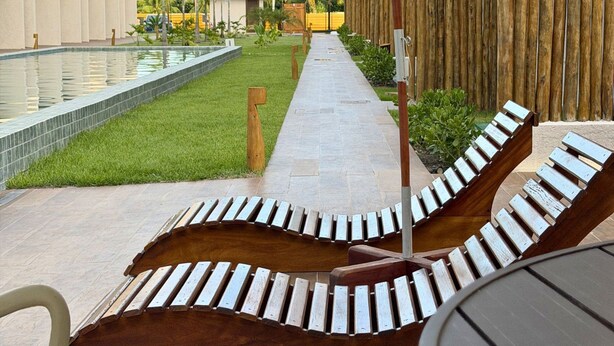 A poolside area with lounge chairs, a wooden fence, and a building with a modern design. - MHV Milagres - Manah B 212 &  B 211  (São Miguel dos Milagres)