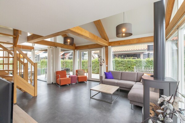 A spacious living area with a sofa, coffee table, and orange chairs. A staircase leads to an upper level. - Wonderful Beach Holiday Home for 6 (Renesse)