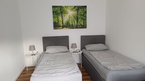 Une chambre à coucher avec deux lits simples, chacun doté d’une table de chevet et d’une lampe. Un grand tableau sur le thème de la forêt est accroché au centre, au-dessus des lits.