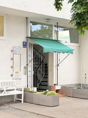 A building entrance with a green awning, a white bench, and a staircase leading to the entrance. - Haus an der Brücke (Munich)
