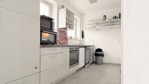 A modern kitchen with white cabinetry, a built-in oven, a microwave, and a trash bin. - Haus an der Brücke (Munich)