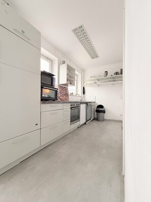 A modern kitchen with white cabinetry, a built-in oven, a microwave, and a trash bin. - Haus an der Brücke (Munich)