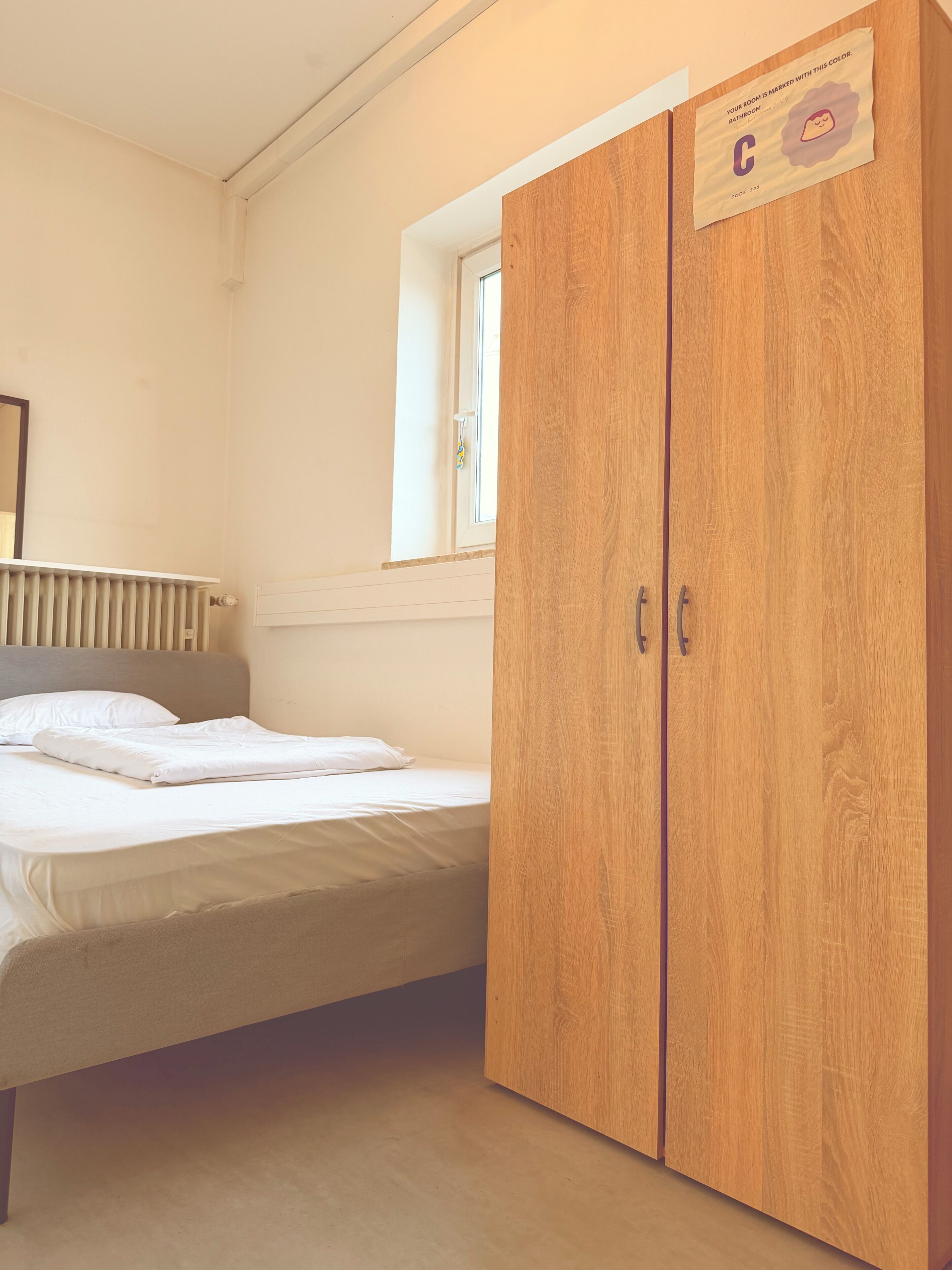 A bedroom with a bed, a wooden wardrobe, a window, and a radiator.