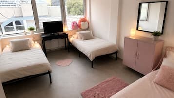 A bedroom with two beds, a desk, a dresser, and a window with blinds.