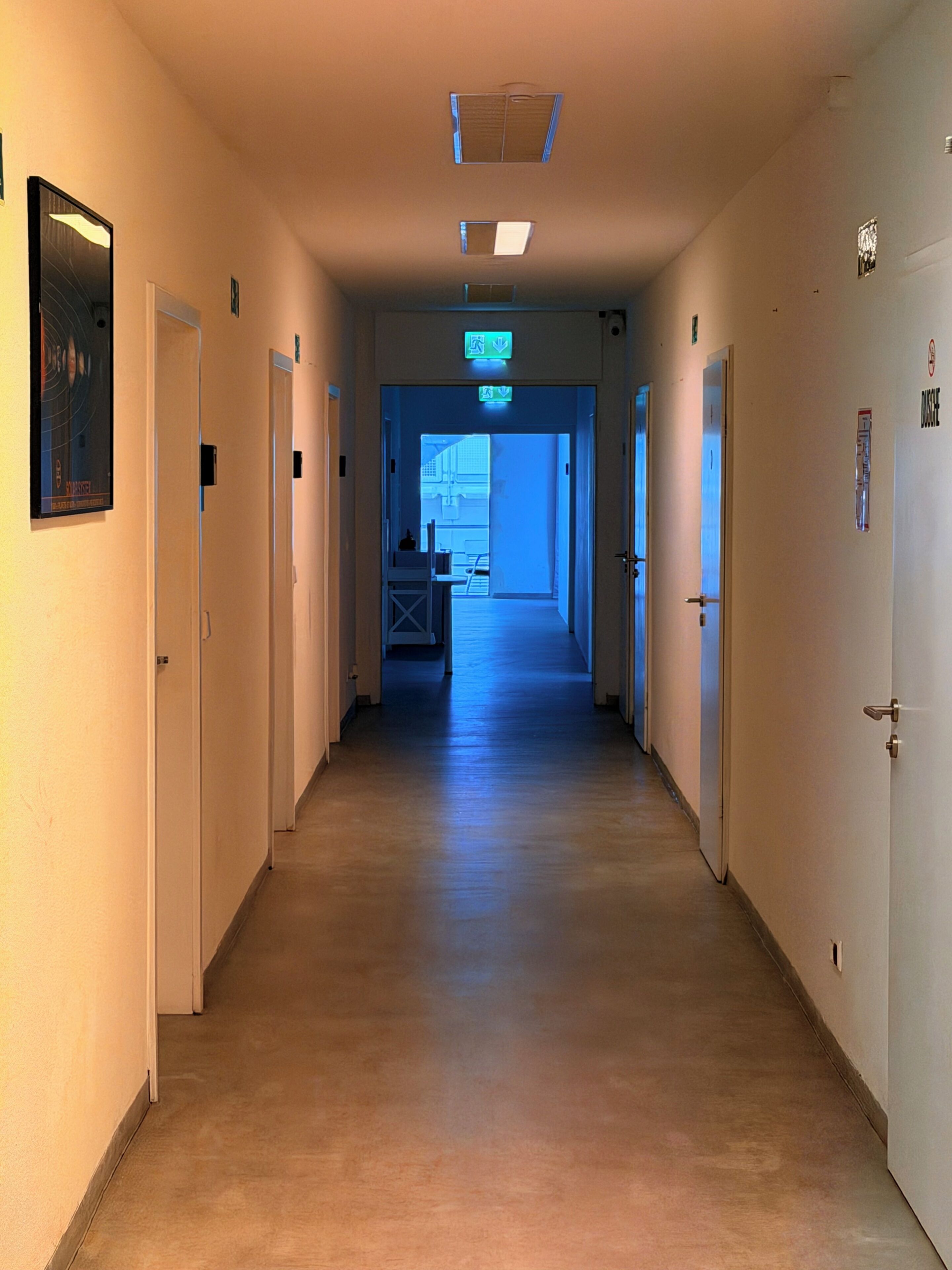 A long, narrow hallway with doors on both sides, leading to a brightly lit room at the end.