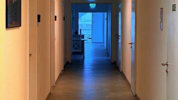 A long, narrow hallway with doors on both sides, leading to a brightly lit room at the end.