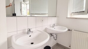 A bathroom with two sinks, a mirror, a window with blinds, and a radiator. - Haus an der Brücke (Munich)