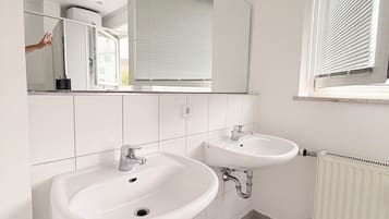 Un baño con dos lavamanos, un espejo, una ventana con persianas y un radiador.