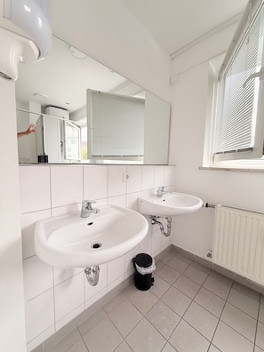 A bathroom with two sinks, a mirror, a window with blinds, and a radiator. - Haus an der Brücke (Munich)
