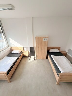A small, modern room with two single beds, a wooden wardrobe, a desk, and a chair. - Haus an der Brücke (Munich)
