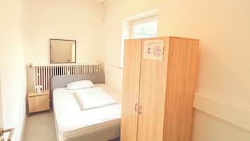 A bedroom with a bed, a wooden wardrobe, a nightstand, a mirror, and a radiator.