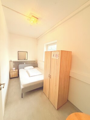 Une chambre à coucher comprenant un lit, une armoire en bois, une table de chevet, un miroir et un radiateur.