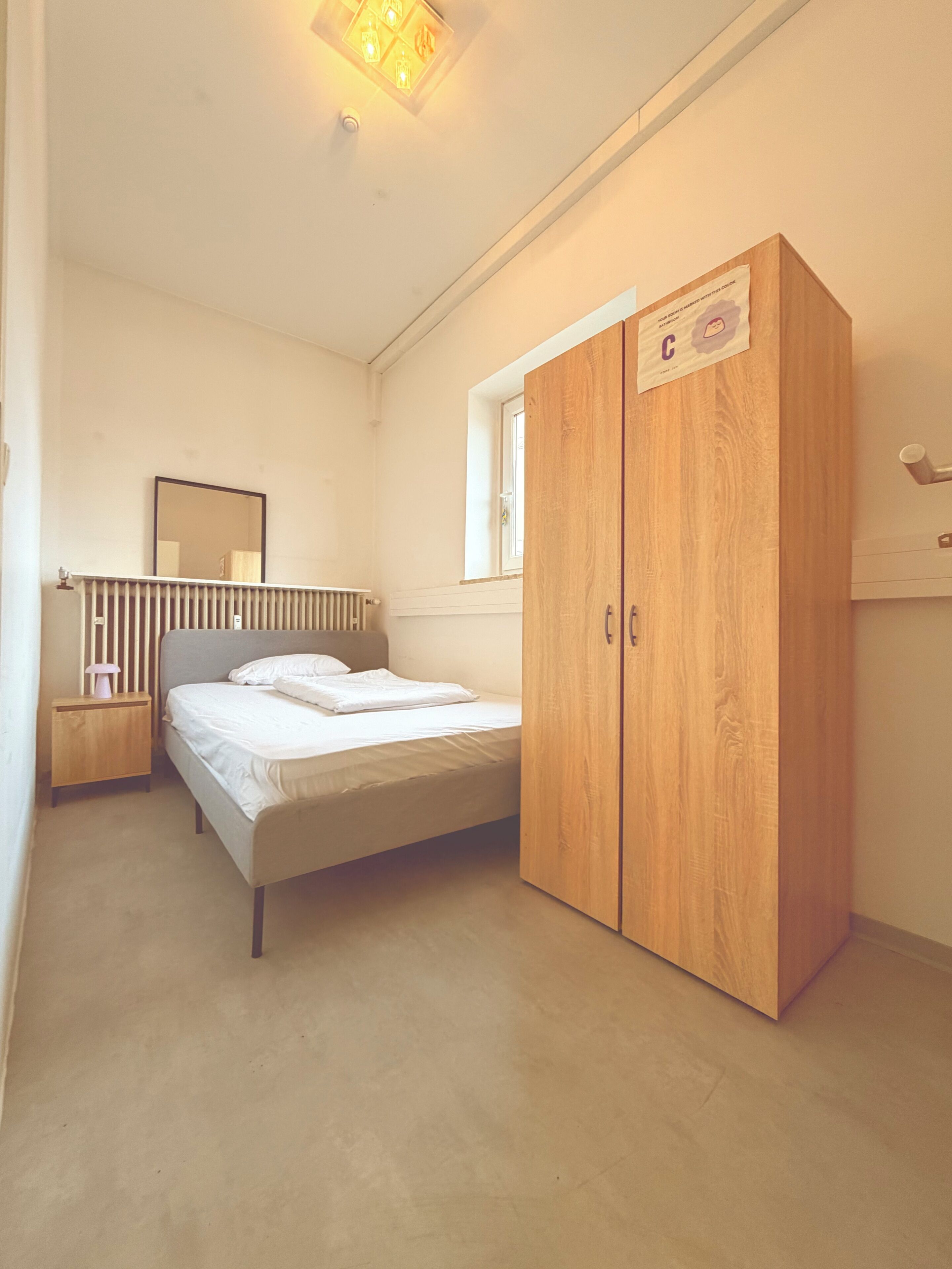 Een slaapkamer met een bed, een houten garderobe, een nachtkastje, een spiegel en een radiator.