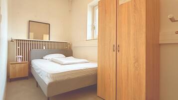 Een slaapkamer met een bed, een houten garderobe, een nachtkastje, een spiegel en een radiator.