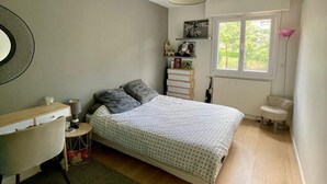 Un dormitorio con una cama, un escritorio, una silla, un radiador y una ventana.
