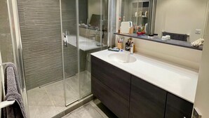 Un baño moderno con cabina de ducha de vidrio, tocador con lavabo y espejo.