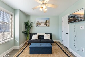 A living room with a ceiling fan, a sofa, a coffee table, a potted plant, and a painting on the wall. - Beautifully Updated Diamond Beach Townhouse (Wildwood)