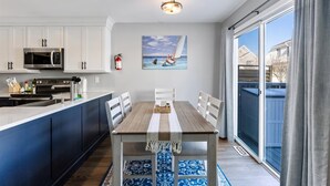 A modern kitchen with white cabinets, a built-in microwave, and a wooden dining table with a white table runner. - Beautifully Updated Diamond Beach Townhouse (Wildwood)