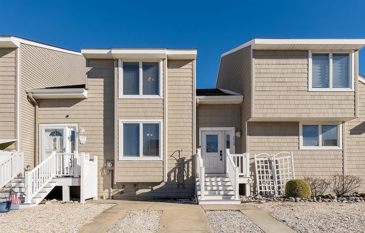 A row of two-story townhouses with a front porch, a small garden, and a clear blue sky.