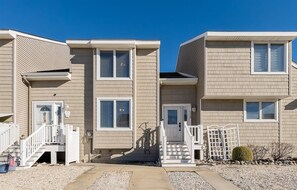 A row of two-story townhouses with a front porch, a small garden, and a clear blue sky. - Beautifully Updated Diamond Beach Townhouse (Wildwood)