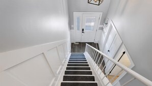 A staircase with white railings and dark carpeted steps leading to a door with frosted glass panels. - Beautifully Updated Diamond Beach Townhouse (Wildwood)