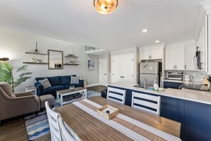 A modern kitchen with white cabinets, a central island, and a dining area with a striped table runner. - Beautifully Updated Diamond Beach Townhouse (Wildwood)