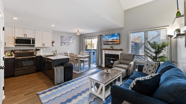 A modern kitchen with stainless steel appliances, a dining area with a table and chairs, a blue and white patterned rug, a blue sofa, and a fireplace. - Beautifully Updated Diamond Beach Townhouse (Wildwood)