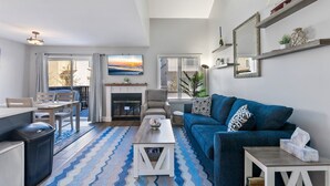 A modern living room with a fireplace, a blue sofa, and a dining area with a table and chairs. - Beautifully Updated Diamond Beach Townhouse (Wildwood)