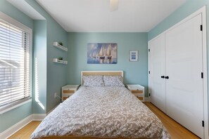 A bedroom with a bed, a nightstand, a dresser, a window with blinds, a painting of sailboats, and a white wardrobe. - Beautifully Updated Diamond Beach Townhouse (Wildwood)
