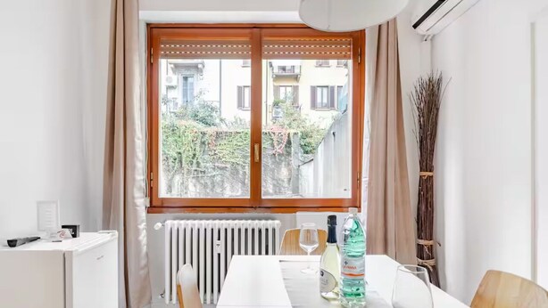 Una cocina moderna con encimera blanca, horno empotrado, refrigerador blanco y una ventana con contraventanas de madera.
