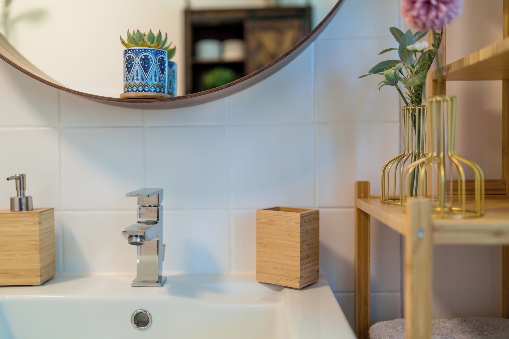 A modern bathroom with a white sink, a chrome faucet, a wooden box, and a vase with flowers.