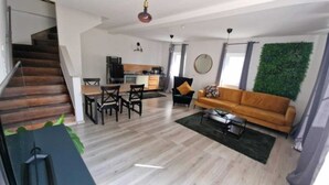 A modern apartment with a staircase, a dining area, a living room with a sofa, and a kitchen.