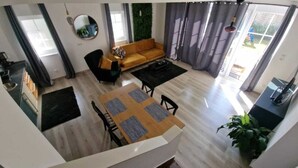 A modern living room with a wooden dining table, a sofa, and a coffee table. There is a kitchen area with a sink and cabinets.
