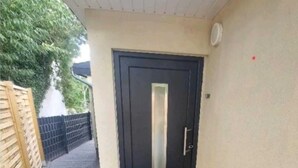 A black door with a vertical handle, a doormat, and a red arrow on the ground.