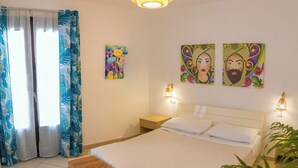 A bedroom with a bed, bedside lamps, a bench, and two paintings on the wall. - Cozy Beach House (Cefalù)