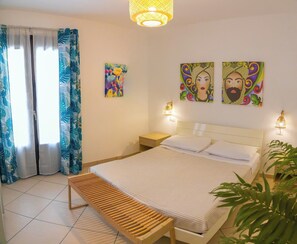 A bedroom with a bed, bedside lamps, a bench, and two paintings on the wall. - Cozy Beach House (Cefalù)