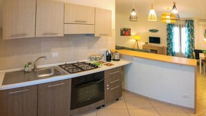 A modern kitchen with a gas stove, sink, and wooden cabinets. There is a small dining area with a table and chairs, and a TV mounted on the wall. - Cozy Beach House (Cefalù)