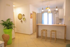 A modern kitchen with a central island, two bar stools, hanging pendant lights, and a potted plant. - Cozy Beach House (Cefalù)