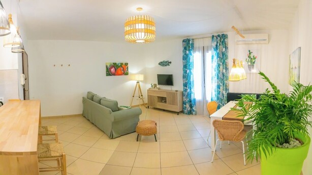 A living room with a sofa, dining table, chairs, a TV, and a potted plant. - Cozy Beach House (Cefalù)