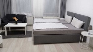 Et moderne hotelværelse med en grå sofa, et hvidt sofabord med en vase, en grå seng med hvide puder og et lille hvidt natbord.