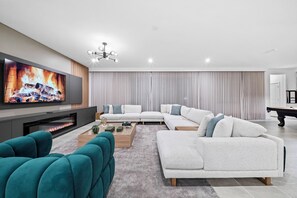 Ein modernes Wohnzimmer mit Flachbildfernseher, Kamin, Ecksofa und Billardtisch.