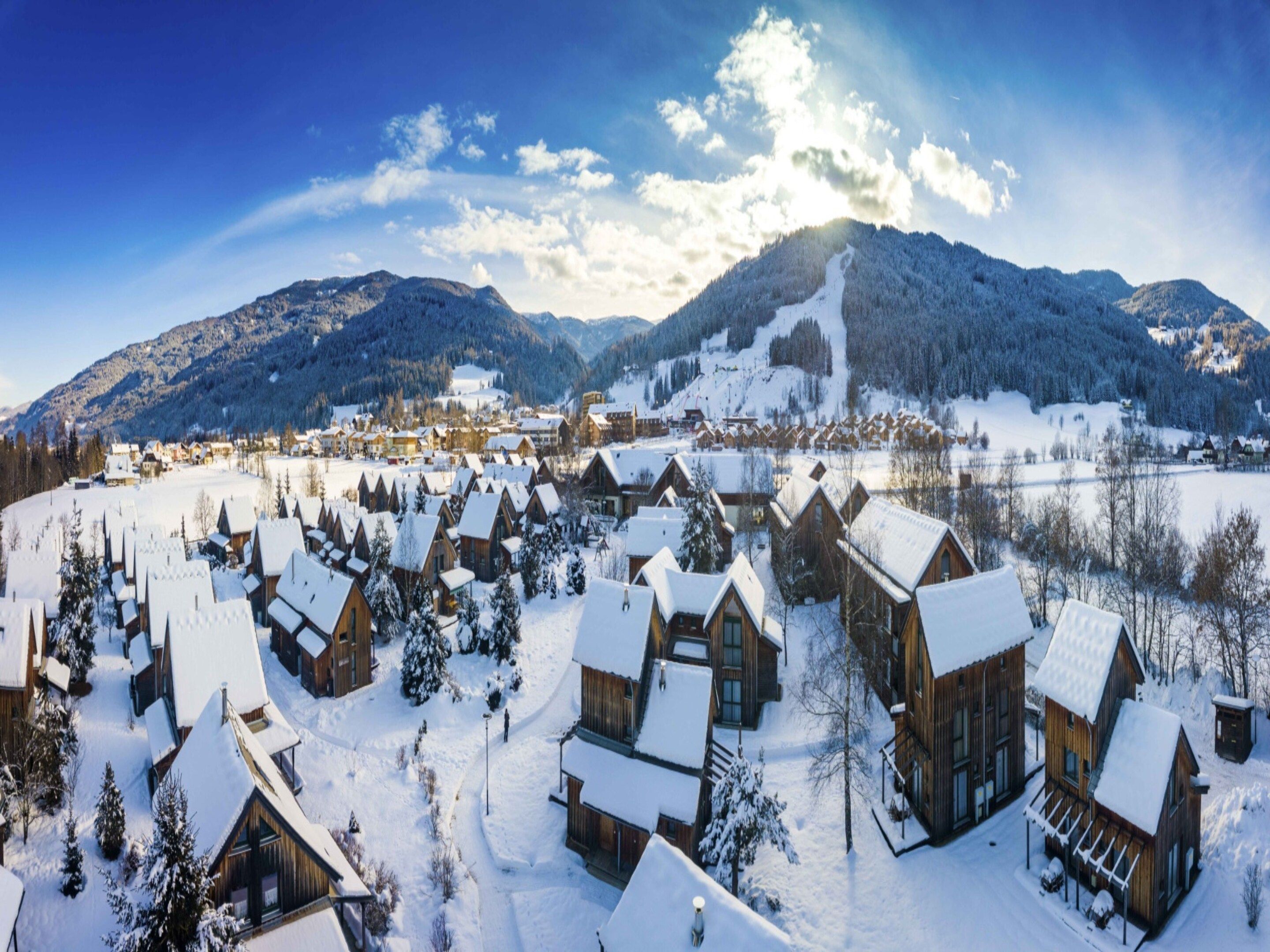 Un pueblo cubierto de nieve con casas de madera y una montaña al fondo.