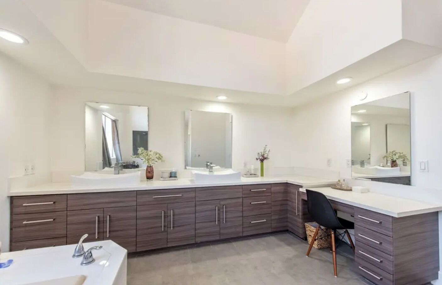 Un baño moderno con tres lavamanos, armarios de madera oscura y un espejo grande.