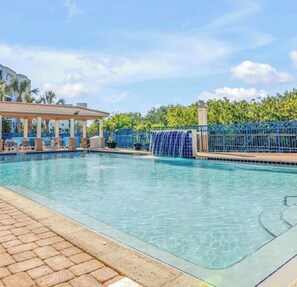 A swimming pool with a water feature, lounge chairs, and a covered area.