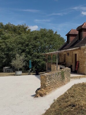 A stone building with a covered patio area, surrounded by trees and a gravel driveway. - Charming stone cottage in Périgord Noir (Saint-Geniès)