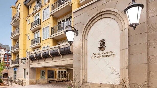 En byggnad med flera våningar och balkonger, en central entré med en skylt som visar texten ”The Ritz-Carlton Club and Residences”, och en gång av tegelstenar som leder till entrén.