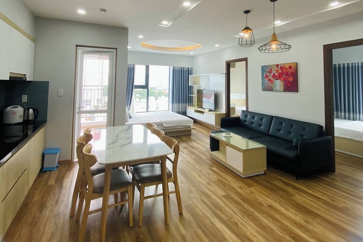 A modern living room with a sofa, dining table, and chairs. There is a TV and artwork on the wall.