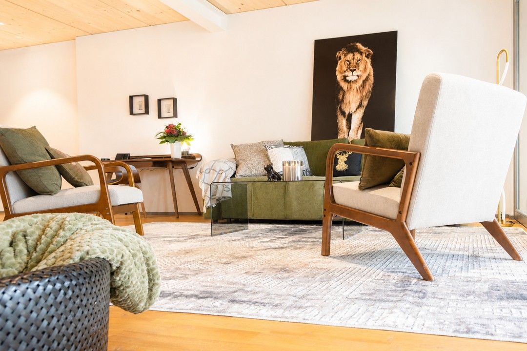 A living room with a green sofa, two armchairs, a coffee table, and a large lion painting on the wall.