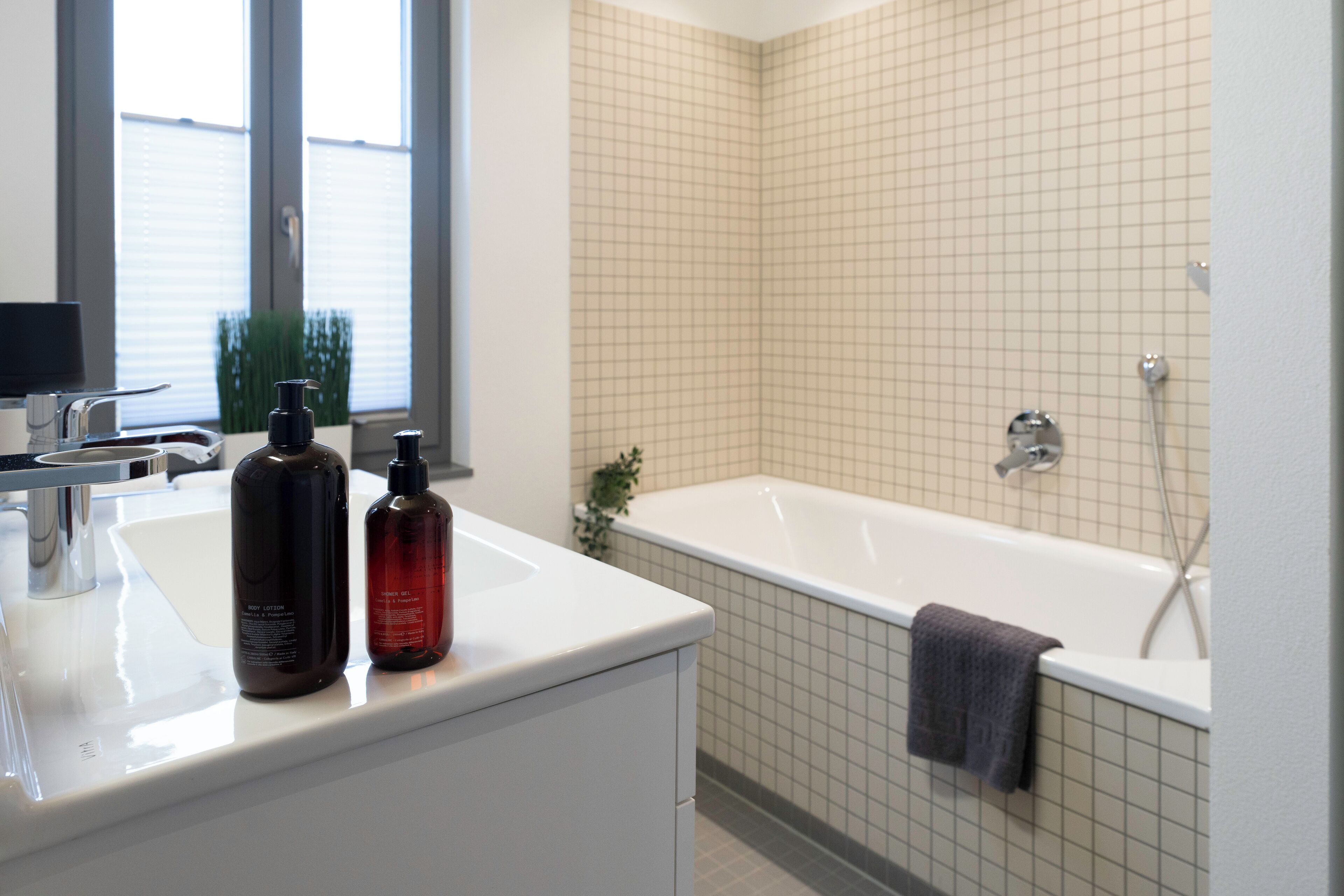 A modern bathroom with a white sink, two bottles of toiletries, a bathtub, and a shower.